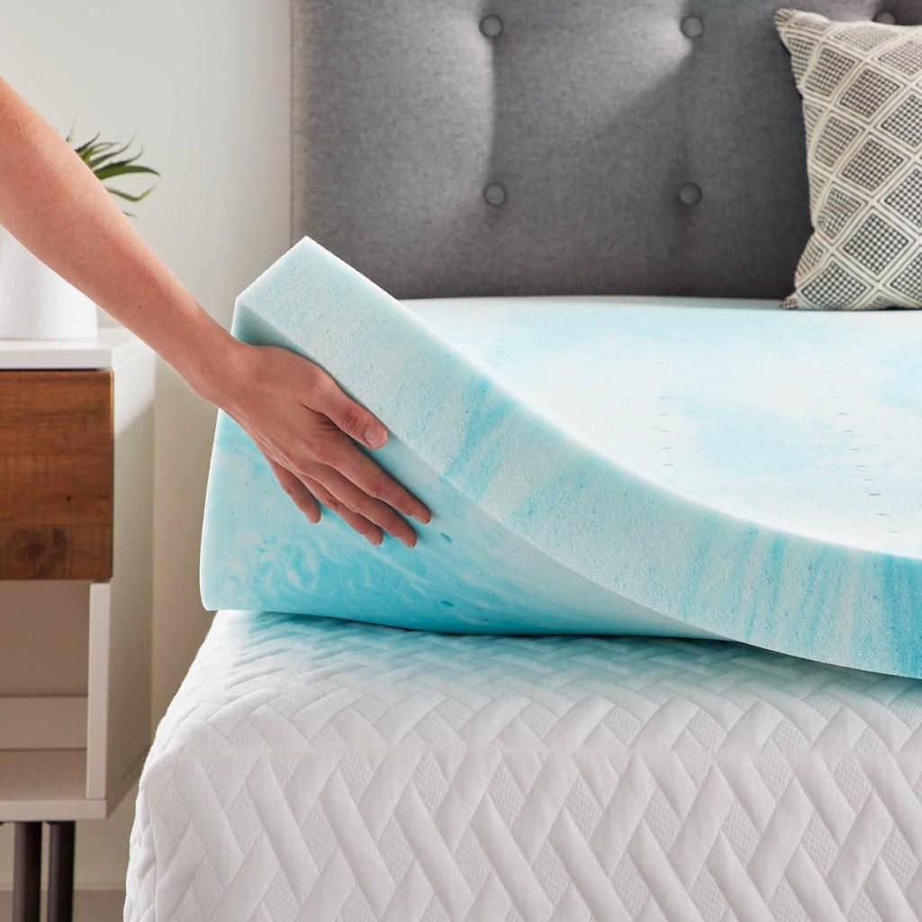 hand lifting up light blue swirl memory foam mattress topper on top of white mattress with grey headboard in bedroom
