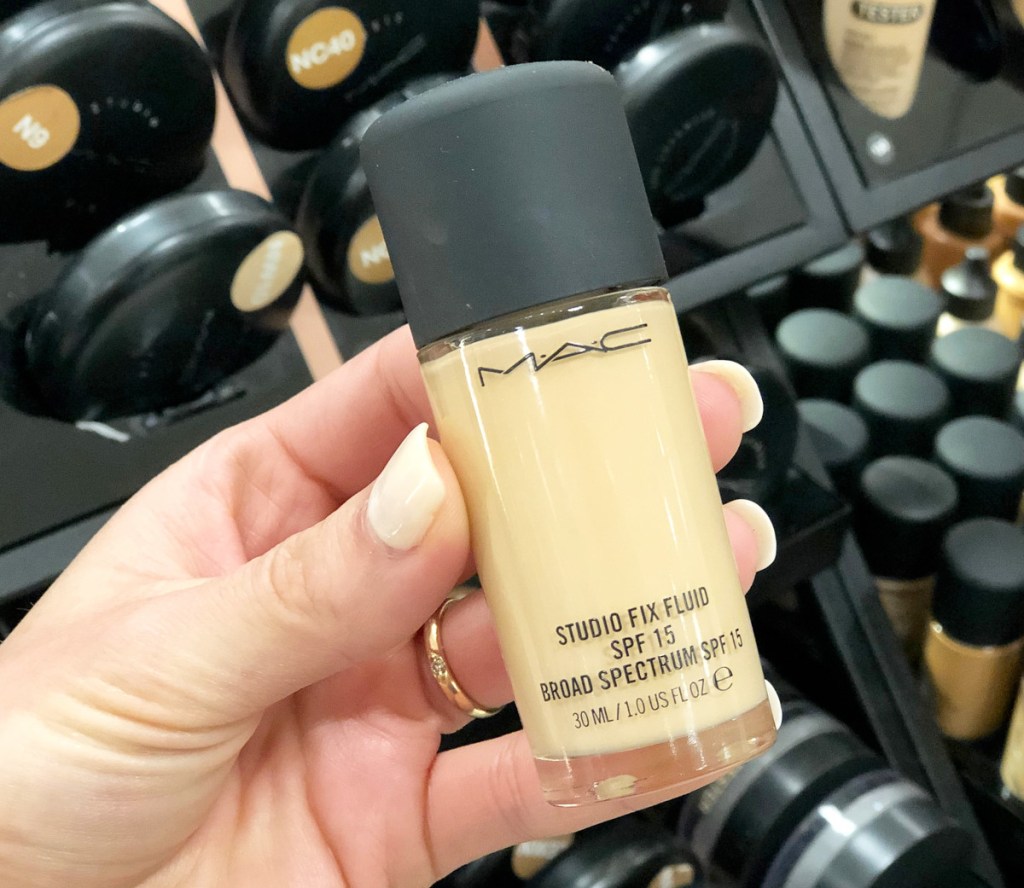 person holding up a bottle of mac liquid foundation with a black lid