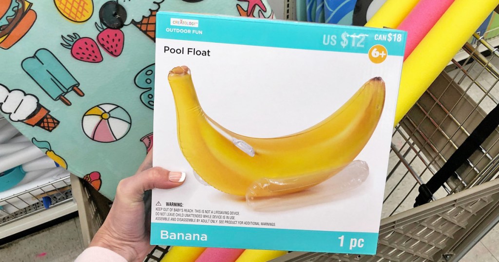 person holding a white and blue box for a banana shaped pool inflatable in front of shopping cart