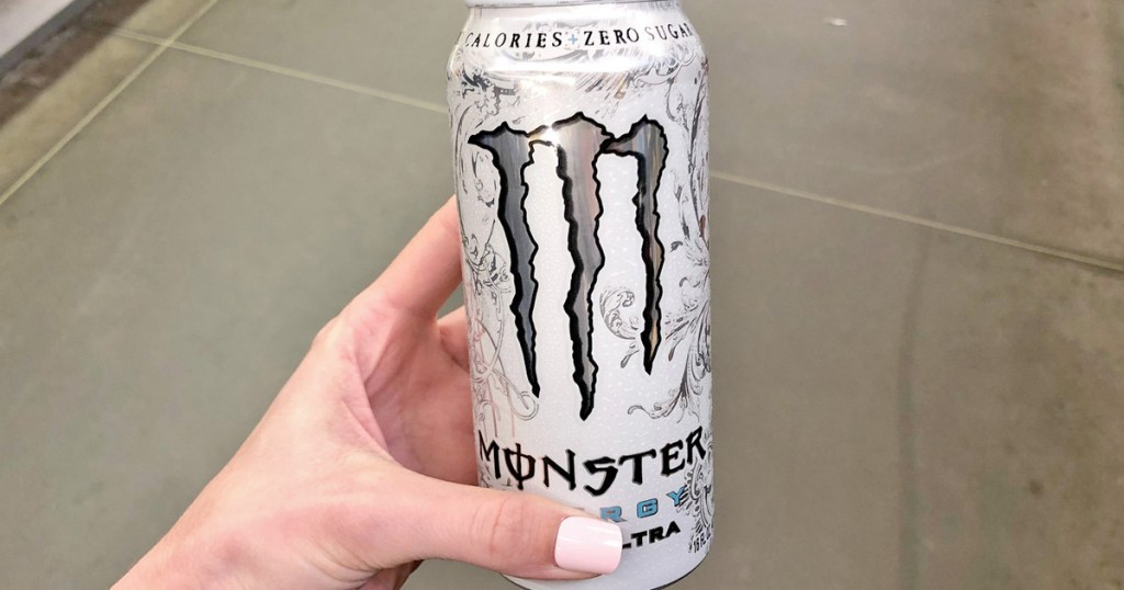 person with light pink nails holding a white can of monster energy drink