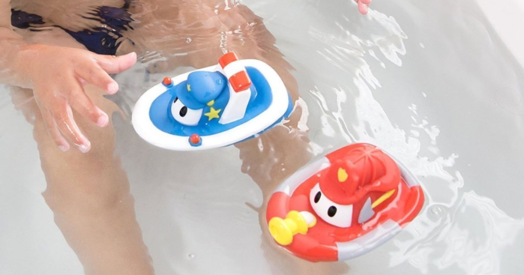 small child sitting in a bath tub full of water playing with rubber tug boats