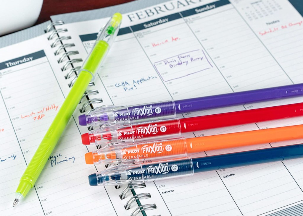 five pens in assorted colored laying on top of a planner