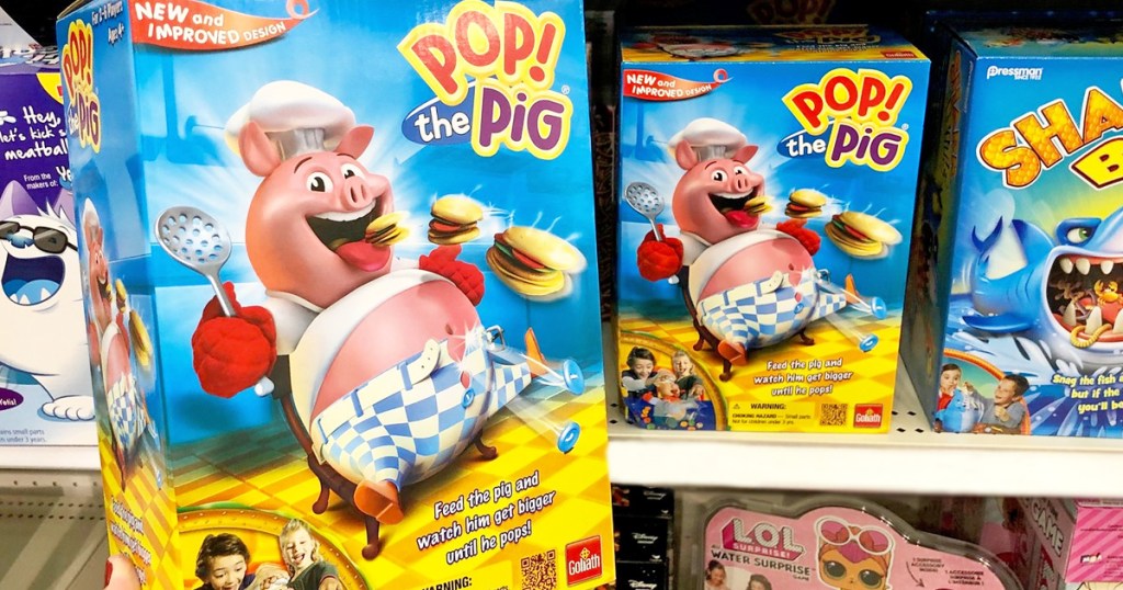 person holding box for Pop The Pig game next to shelf with other kids games