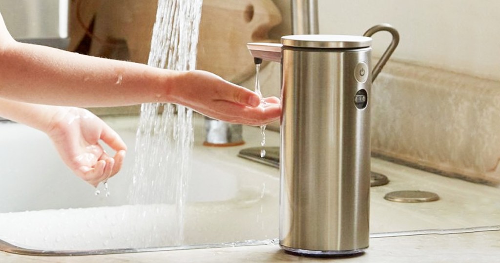 person putting hand under sensor soap dispenser with running water in background