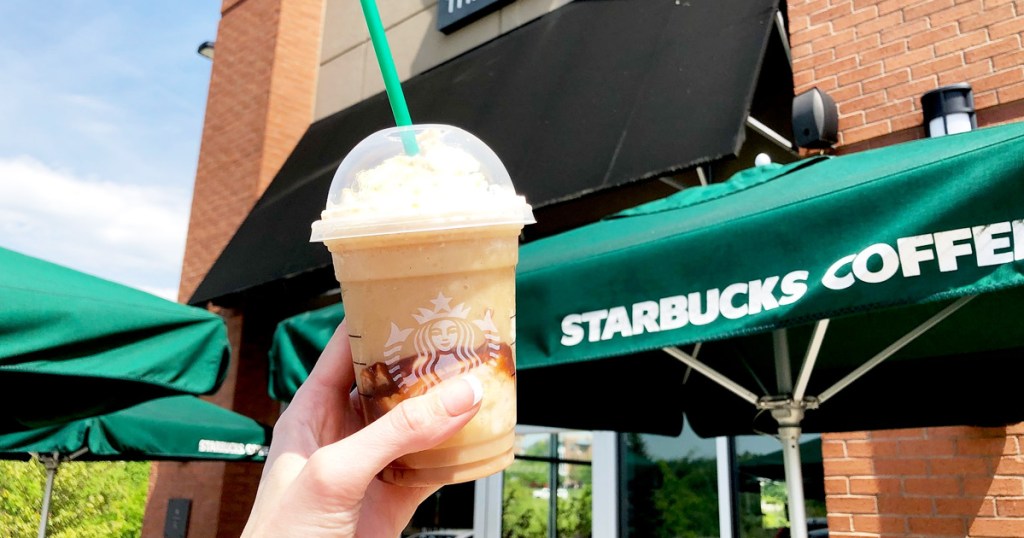person holding up frappuccino drink outside of starbucks store with green umbrella