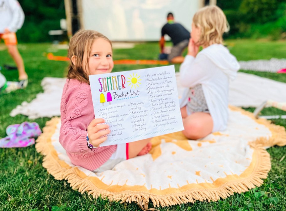 Little girl holding up her free printable summer bucket list
