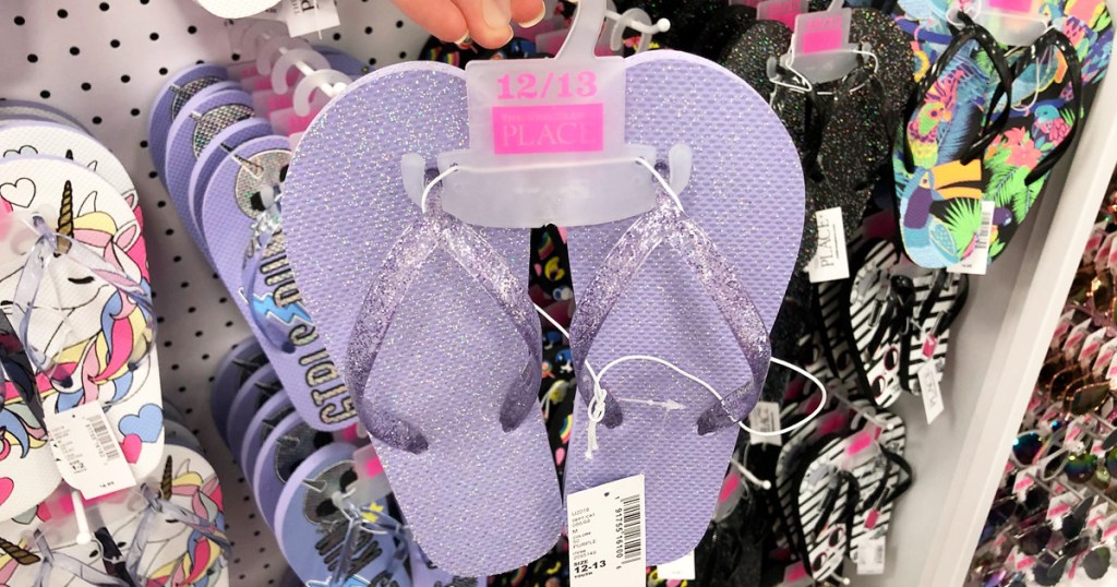 person holding up a pair of purple glitter flip flops