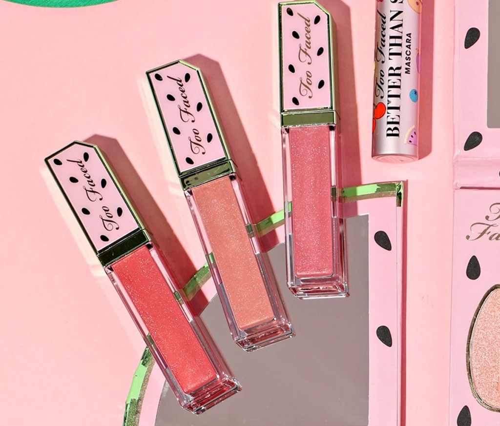 three shades of pink lip gloss with watermelon printed lids on a pink background