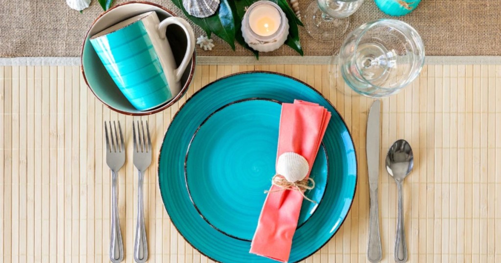 turquoise dinnerware and utensils on table with seashells and candle