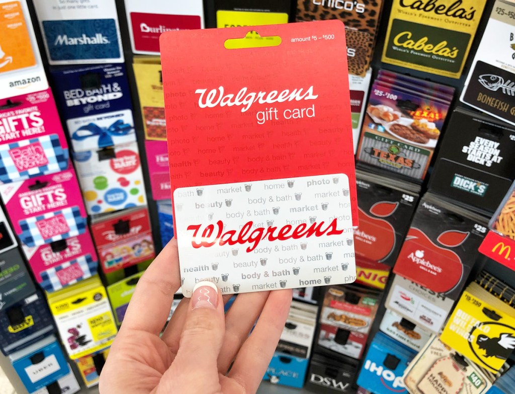 person holding up a white and red walgreens gift card in from of display of gift cards