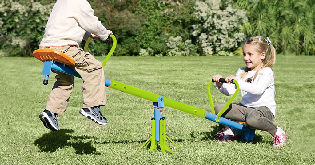 boy and girl playing on green seesaw toy on grass