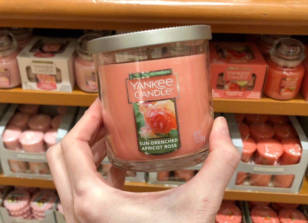 person holding up a pink yankee candle in the scent apricot rose