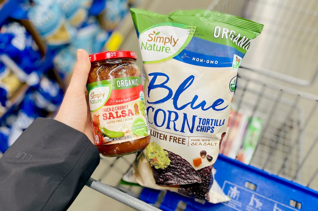 hand holding a jar of organic salsa next to bag of blue corn chips in aldi cart
