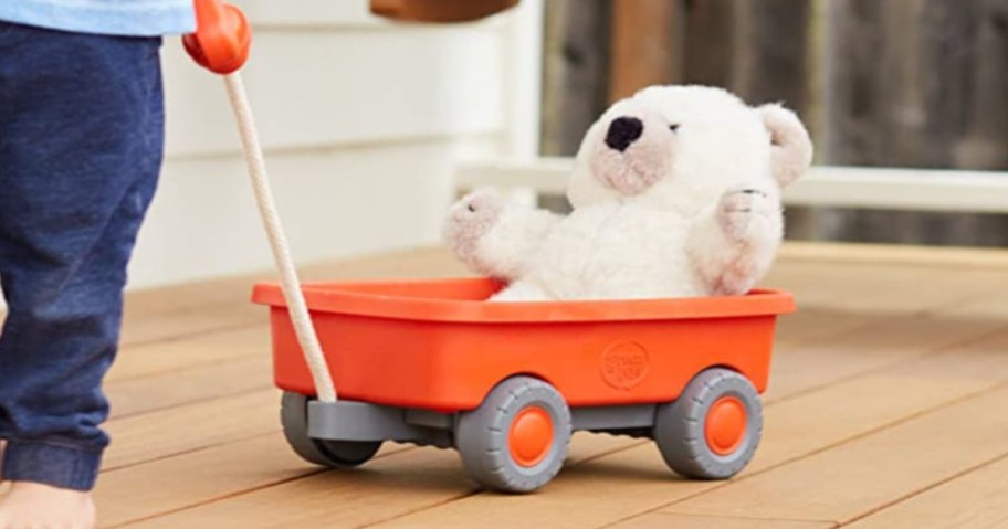 Little kid pulling orange wagon with bear in it