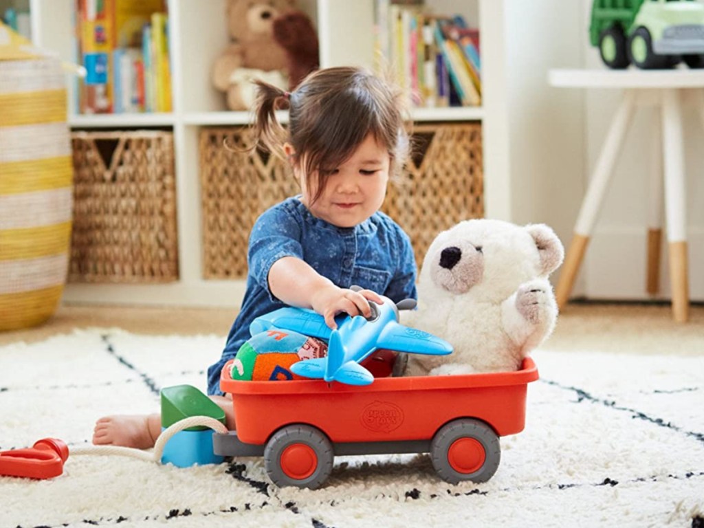 little girl putting toys in an orange wagon