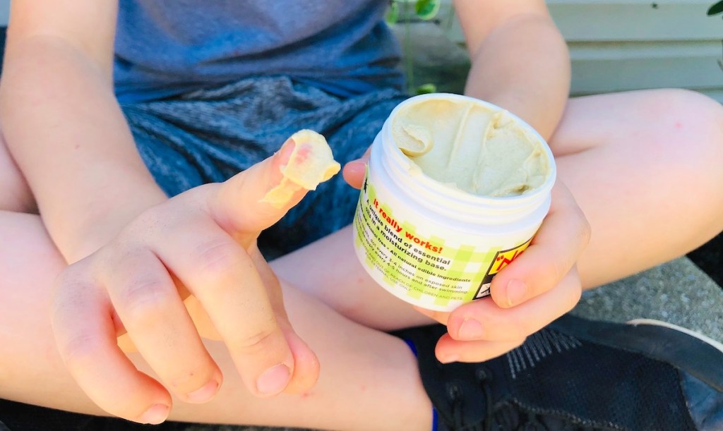 kid with bug repellent lotion on finger tip holding jar