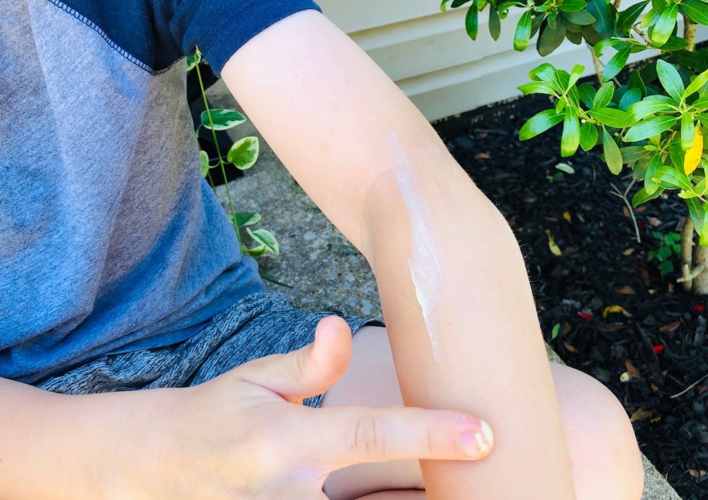 kid putting lotion on arm with finger