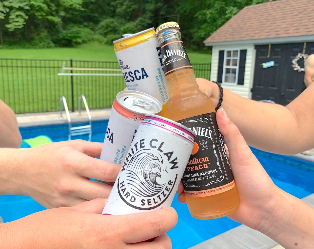 hands holding multiple alcoholic drinks cheers in front of pool