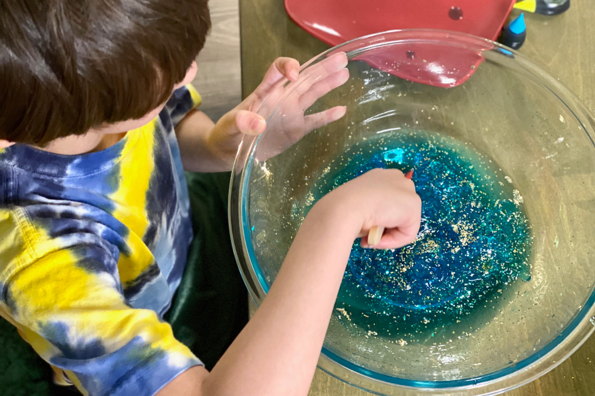 Child mixing DIY slime mix in glass bowl