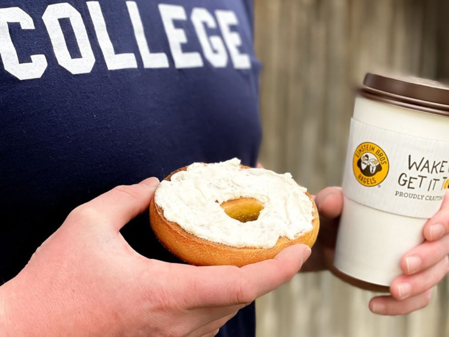 person with a tee shirt that says college holding a bagel and coffee