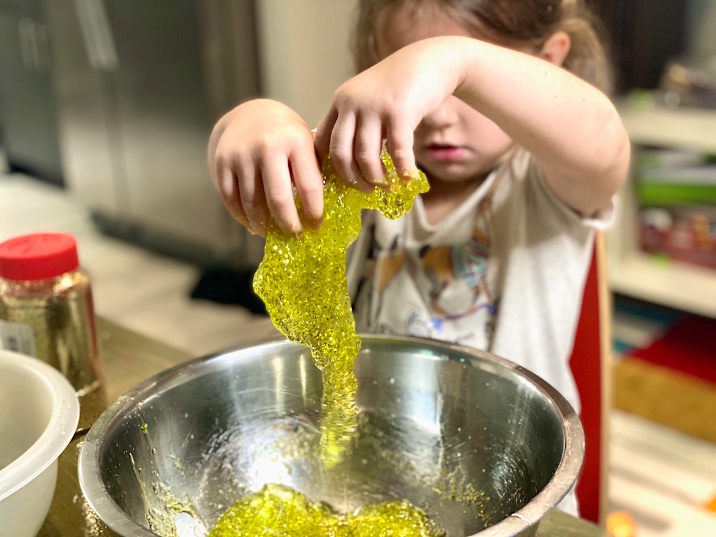 little girl playing with green slime with glitter in bowl