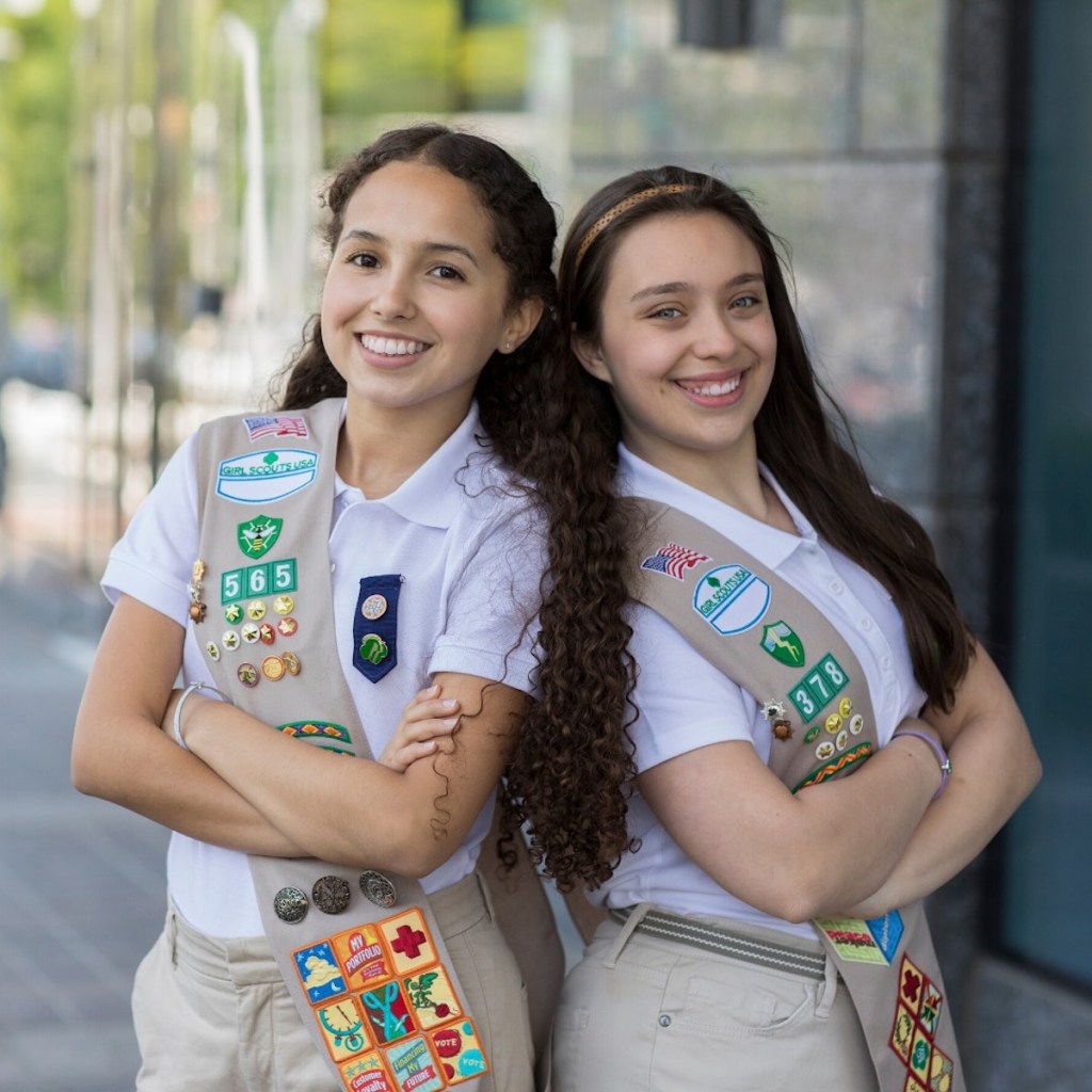 two girl scouts standing back to back smiling