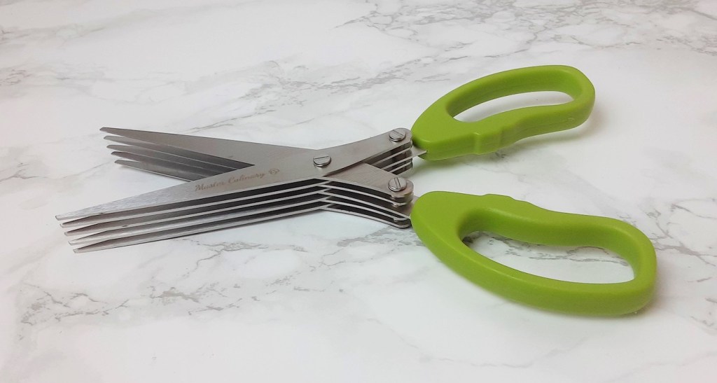 multi blade scissors with green handles sitting on marble countertop