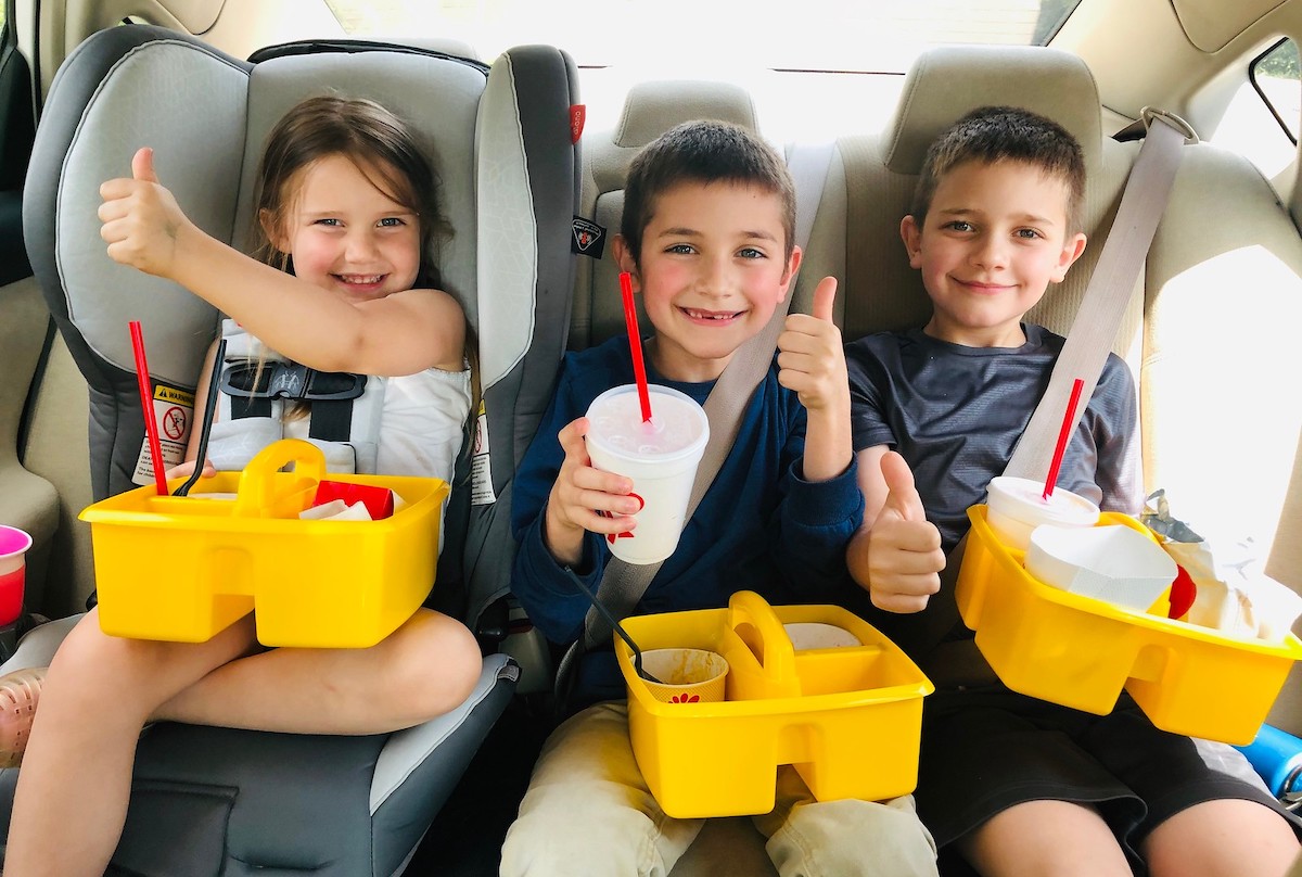 three kids sitting in car with yellow caddies and fast food on lap