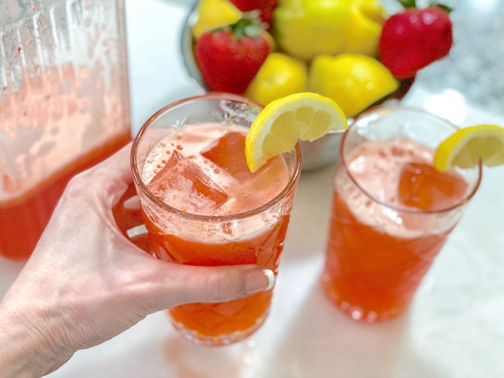 Hand holding a glass of strawberry lemonade with lemon garnish