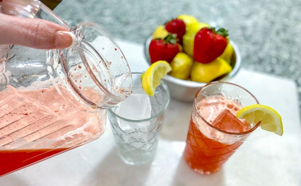 Hand pouring strawberry lemonade into drinking glasses with lemon garnishes