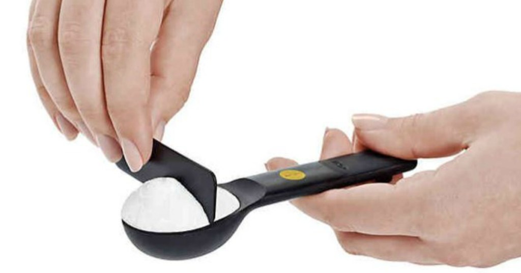 hand holding measuring spoon while other hand levels powder