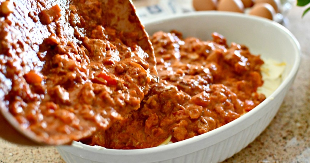 pouring meat sauce on spaghetti casserole