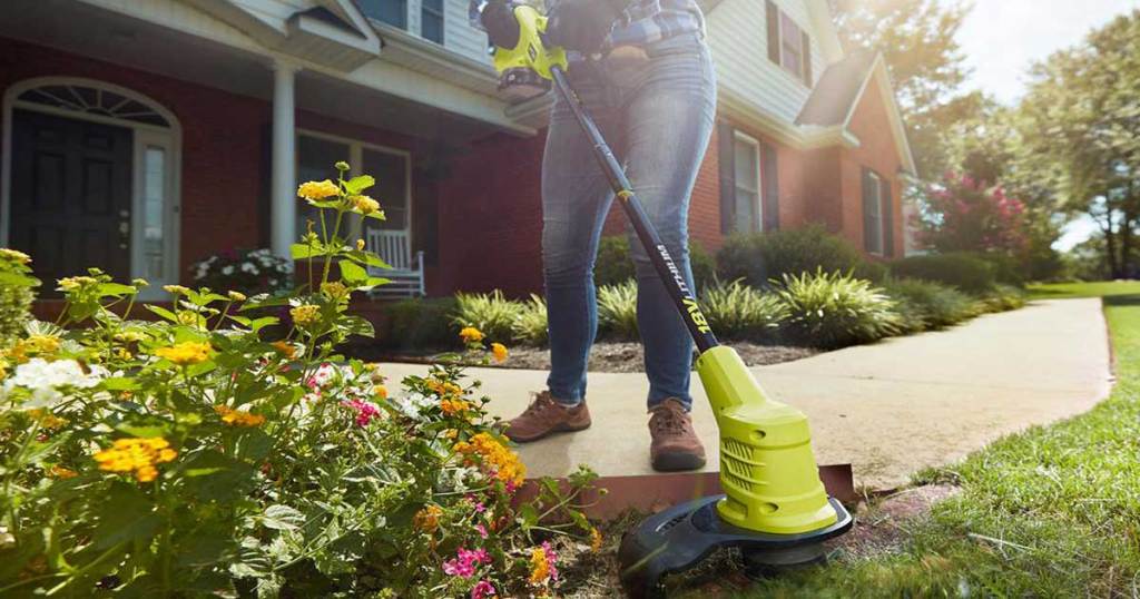 person using a lawn trimmer on a yard in front of a house