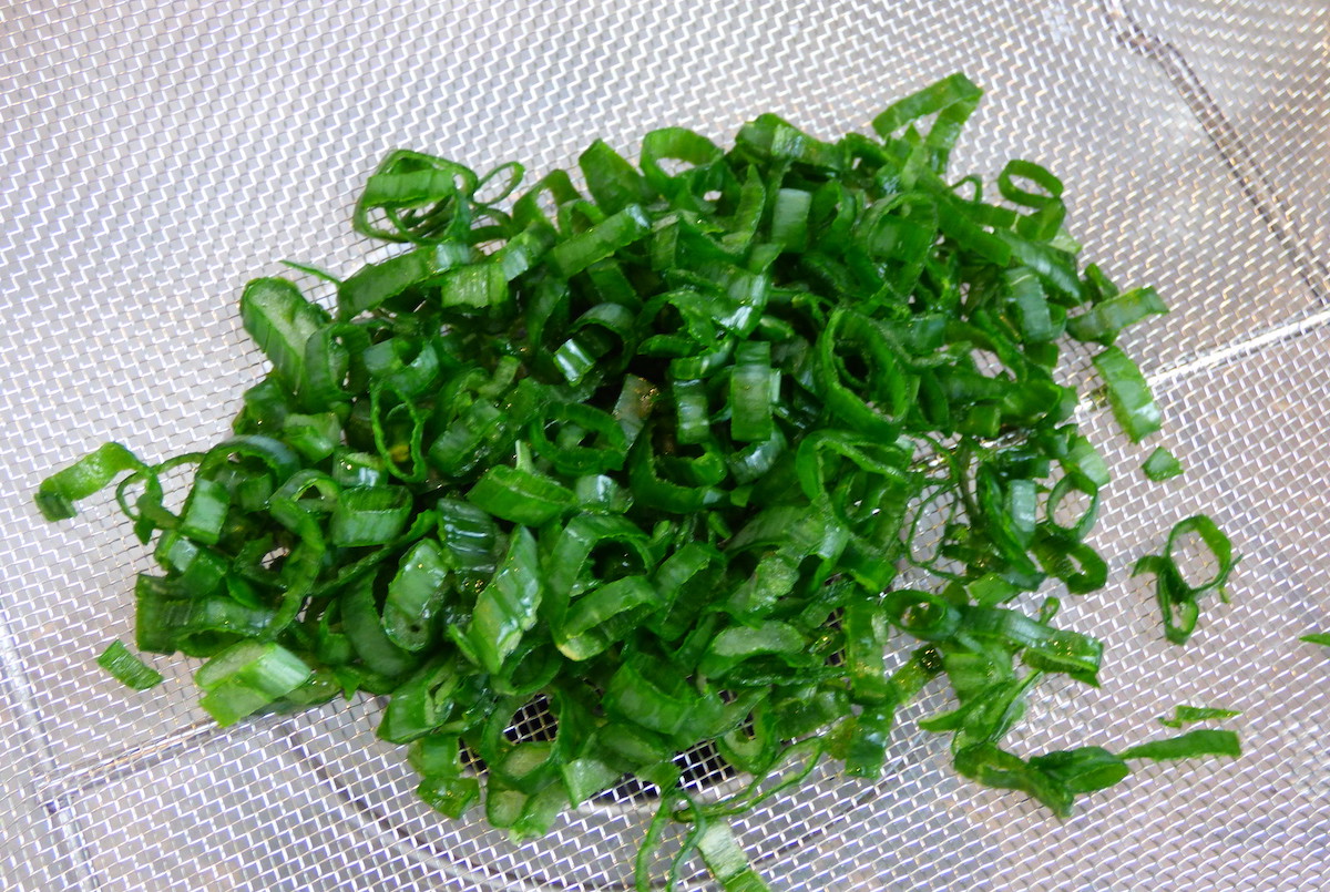 pile of fresh green scallions in metal strainer