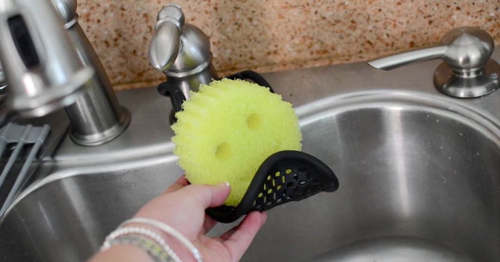hand holding a black sponge holder with round yellow smiley face sponge