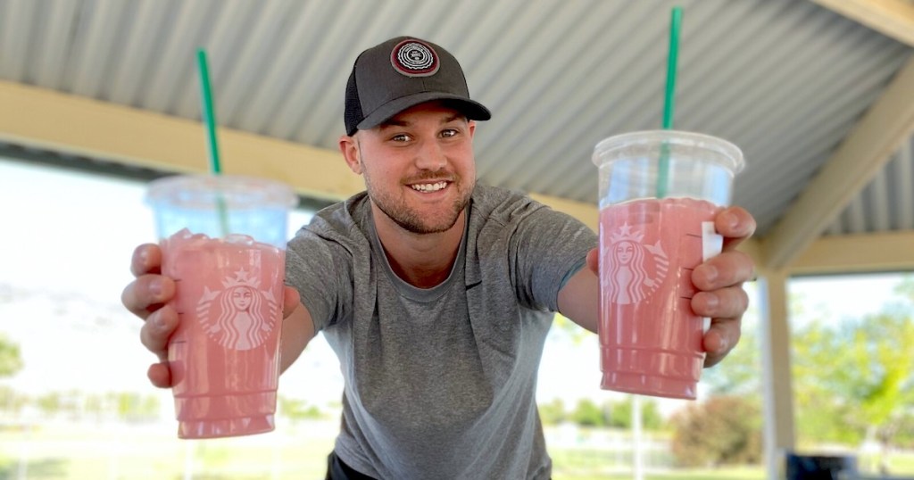 man holding two pink starbucks drink with green straws