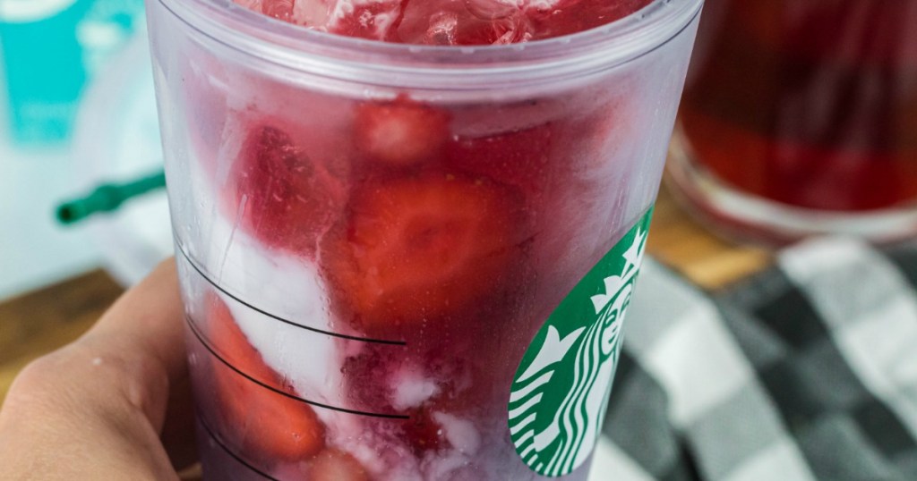 holding Starbucks inspired pink drink with fresh strawberries 