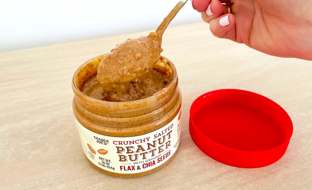 close up of hand holding spoon in trader joes crunchy peanut butter