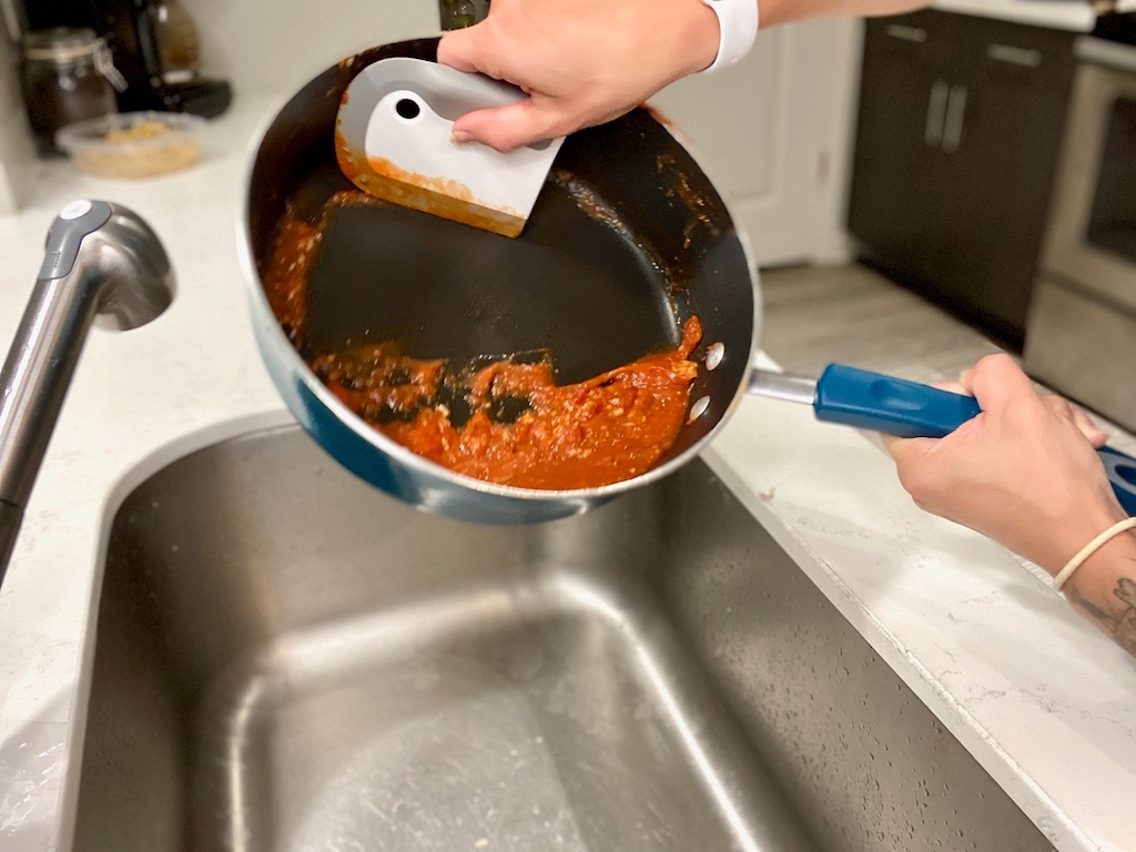 using dish squeegee to clean sauce out of pan 