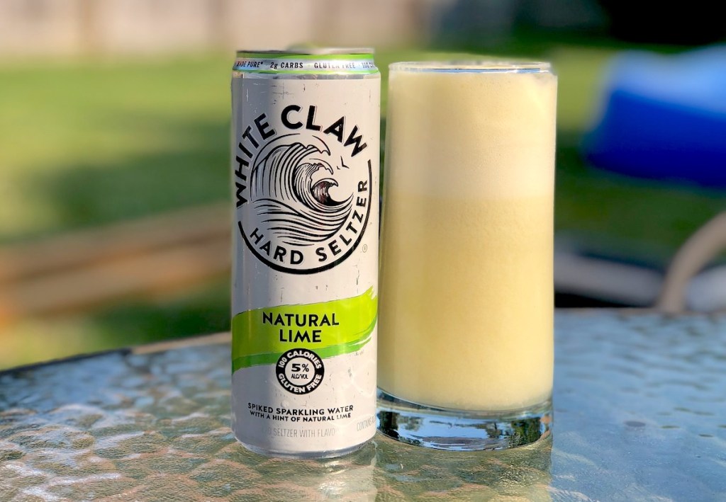 white claw natural lime can and glass with slushie sitting on glass tabletop outside
