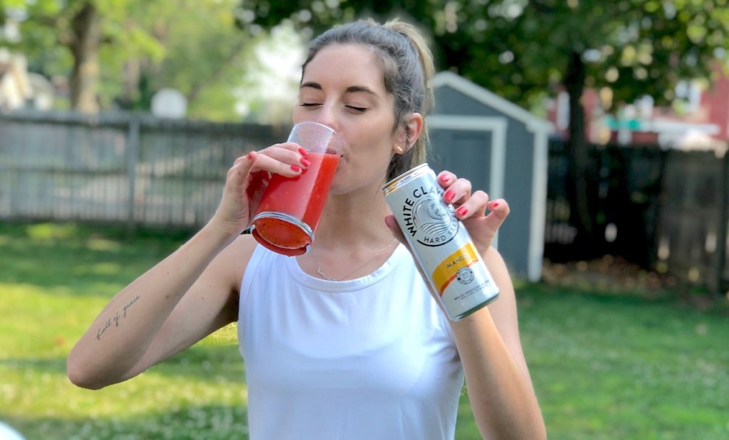 woman standing outside drinking from clear glass with red white claw slushie