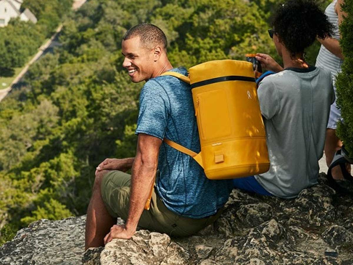 man hiking with a yellow backpack cooler on a mountain