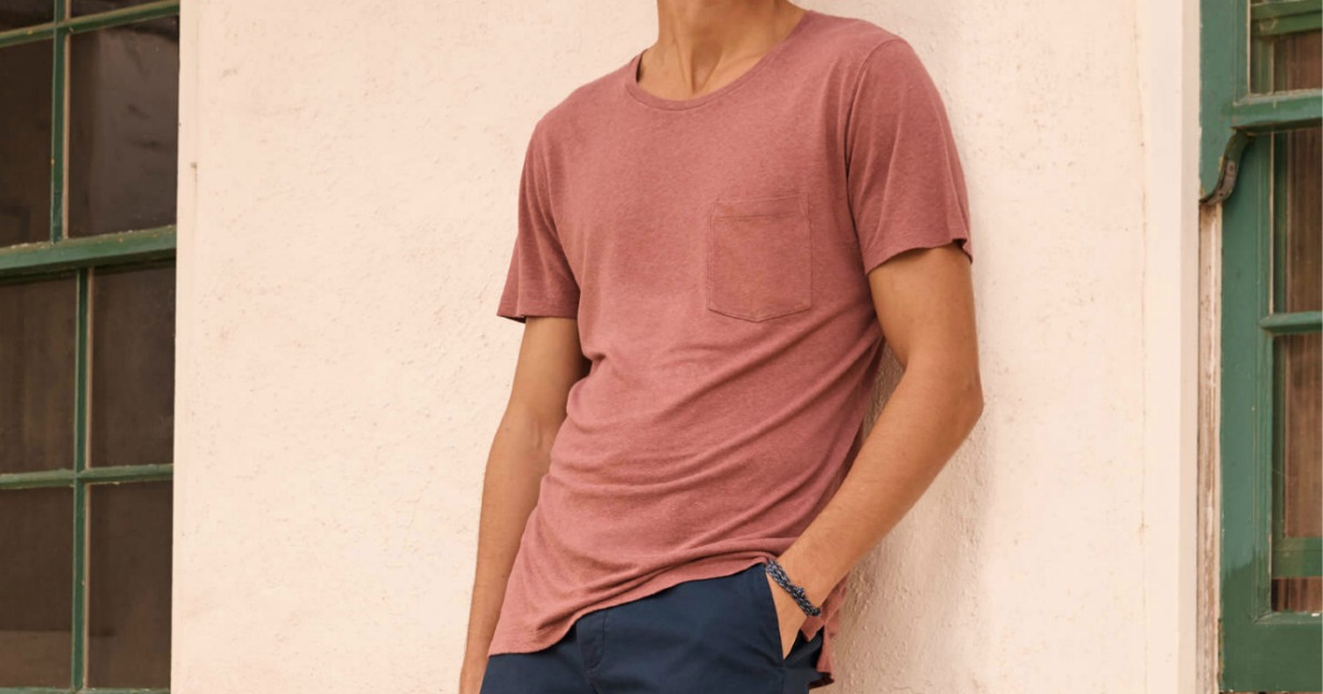 Man leaning against a wall wearing a pink colored tee