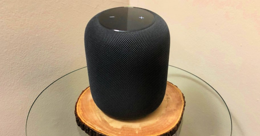 apple homepod sitting on a wooden disk on a small glass table