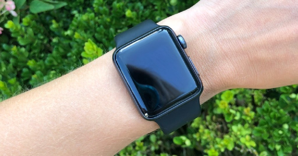 arm with black Apple watch and greenery in background