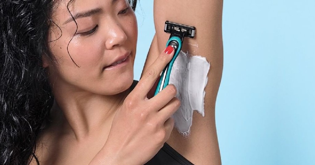 woman shaving armpit with teal razor and shaving cream