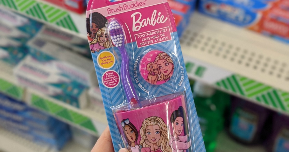 Hand holding a Barbie themed toothbrush set near in-store display