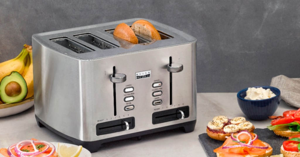 four sliced bella professional toaster with bagel in two of the spots with random food around the table