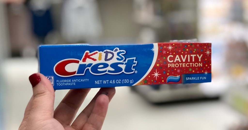 woman's hand holding tube of kids toothpaste with blurred store background