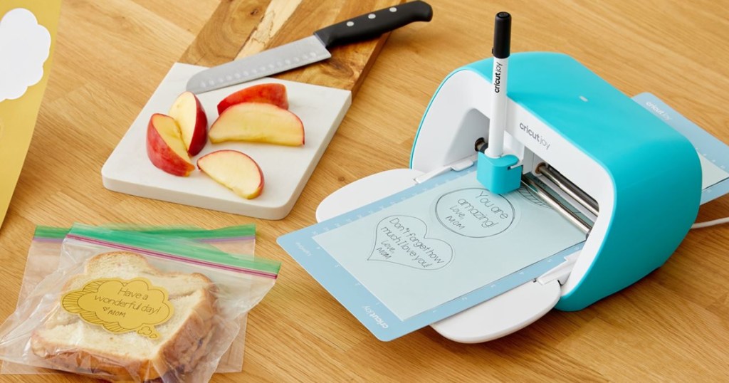 Cricut Joy sitting on a countertop next to sliced apples and Sandwiches